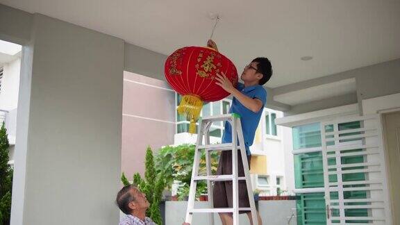 亚洲华人父亲在除夕夜在他们家的前院给儿子递红灯笼