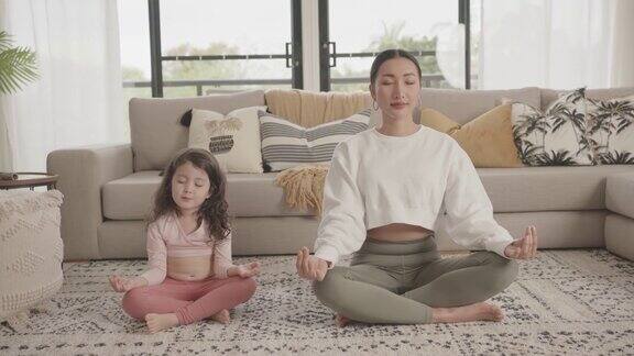 亚洲母亲和混血亚洲女儿在家练习瑜伽在线流课程家庭在线学习一起健康的生活方式健康的理念