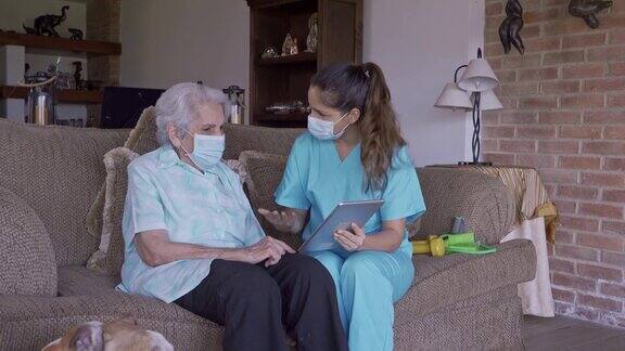 西班牙年轻护士在家里向高级妇女解释数字平板电脑的医疗结果
