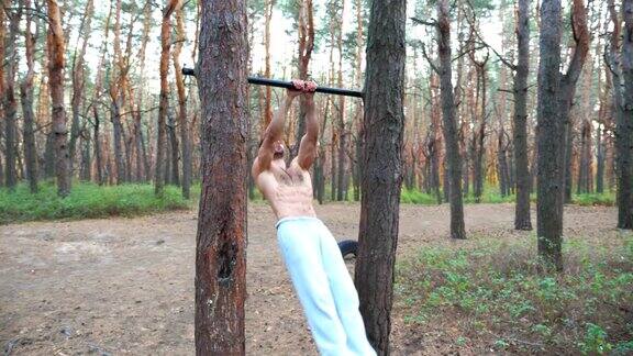 运动员在单杠上训练腹部肌肉举起身体在森林里锻炼的肌肉男运动员的户外锻炼运动和积极的生活方式慢镜头摄影