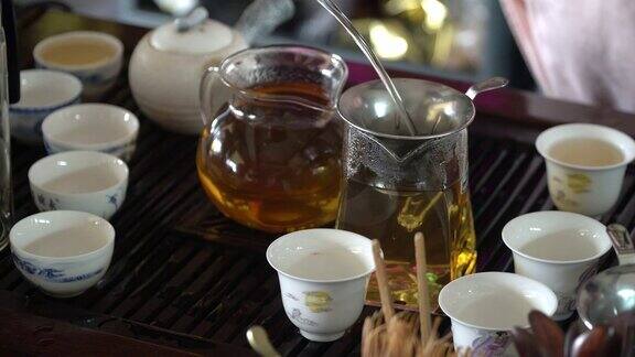 中国茶道女人的手拿起茶壶把热茶倒进桌子上放着陶瓷茶杯的玻璃杯里4k视频