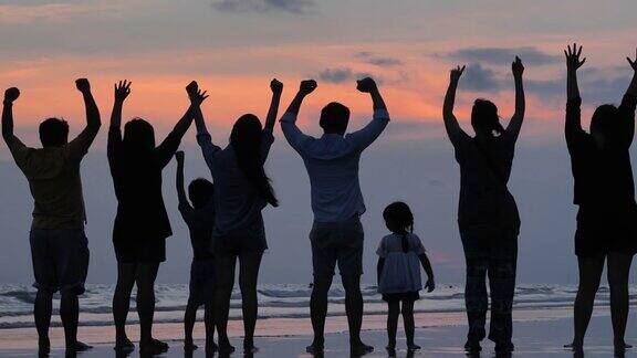 后视图在剪影快乐的多代八口之家举起双臂一边看风景一边张开双臂享受日落沙滩上的旅行假期张开双臂