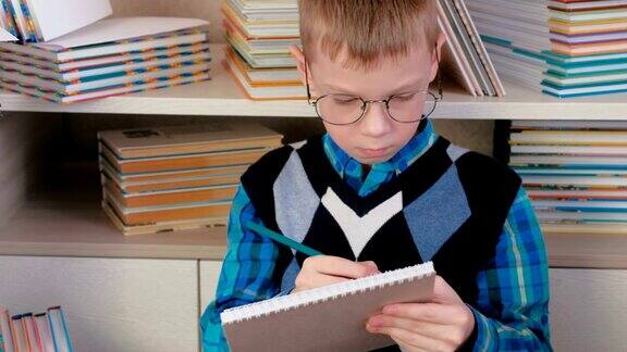 一个七岁的戴眼镜的小男孩坐在书堆里的速写本上画着什么特写镜头