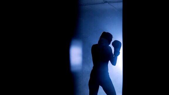 一个女拳击手在黑暗的体育馆训练的剪影