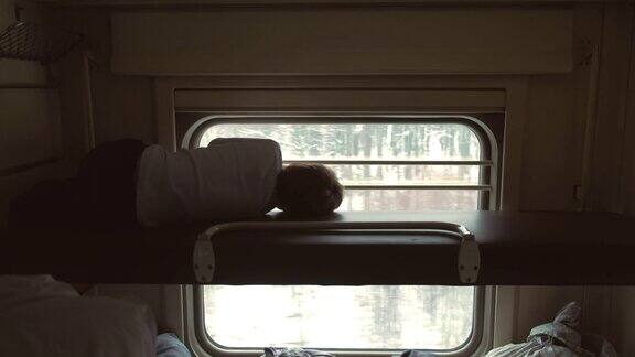 火车上的男孩躺在二等车厢的顶层架子上望着窗户后视图