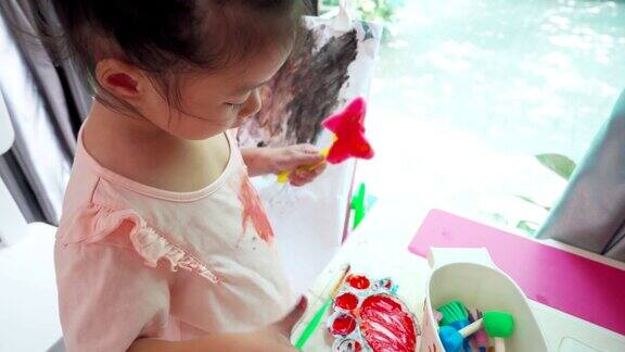 亚洲女孩站着在游戏室的画架上画她的衬衫白色的画布在纸上画蝴蝶海绵邮票孩子们的创造力绘画过程的特写镜头