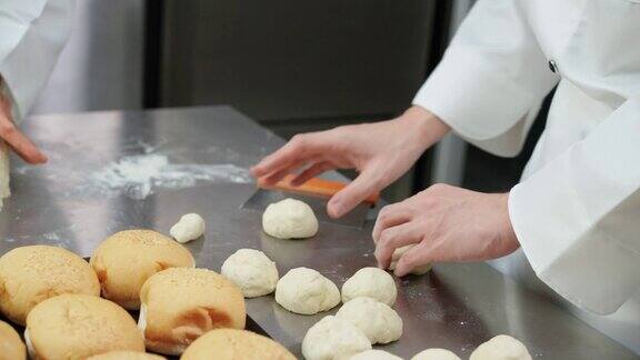 近距离:在前面的烤箱烤面包而厨师在塑形前将面团分成相同大小厨师揉面和准备面团在商业烘焙厨房制作面包和面包