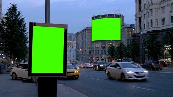 两块带有绿色屏幕的广告牌晚上在一条繁忙的街道上