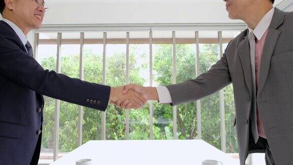 两个商人近距离站起来在会议室里互相握手处理商务协议