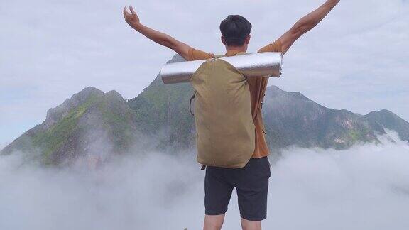 亚洲男徒步旅行者徒步到雾山之巅举起双手庆祝