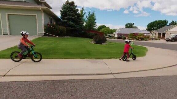 两名白人男孩(五岁和四岁)戴着自行车头盔在多云的天空下骑着自行车穿过居民区