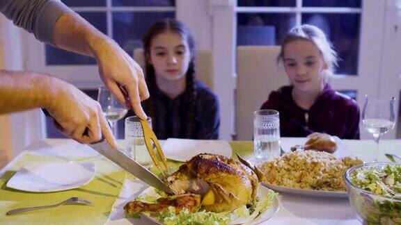 男人在节日餐桌上切鸡把鸡腿放在女儿的盘子里