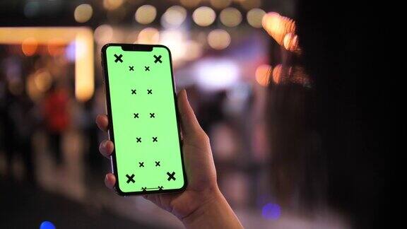 一名女子晚上在街上拿着绿屏智能手机