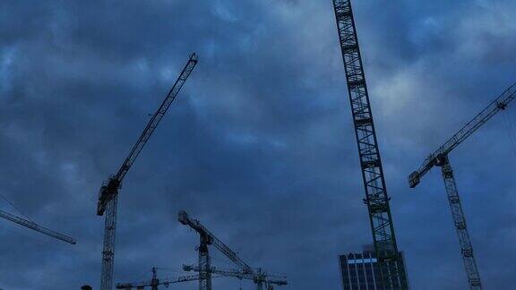 黑暗多云的天空上的建筑起重机日落后工地