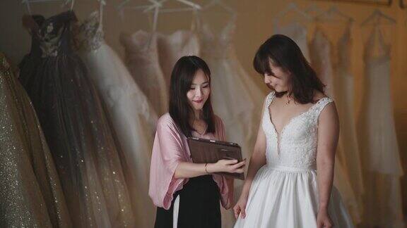 亚洲的中国女新娘商店老板向她的顾客解释新娘使用数码平板选择套餐定价定制设计的婚纱