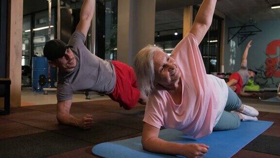年轻的私人教练协助他的老年病人在瑜伽垫上练习