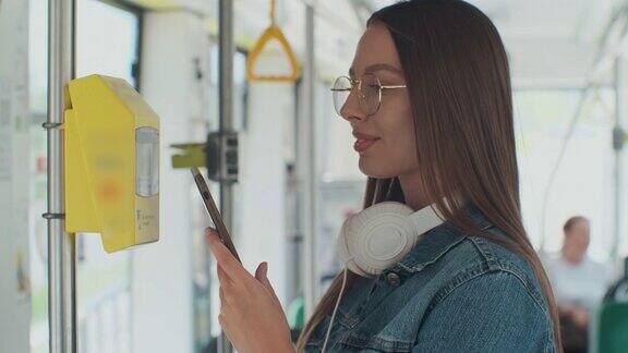 一个微笑的年轻女子用智能手机在无接触的情况下购买有轨电车中的公共交通工具