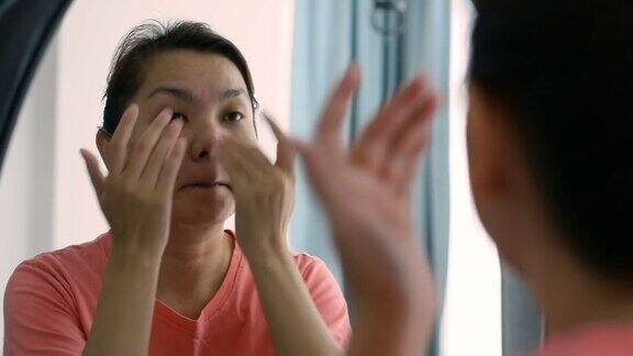 中年亚洲妇女在镜子中涂抹面霜妇女护理她的皮肤和脸上的皱纹皮肤护理