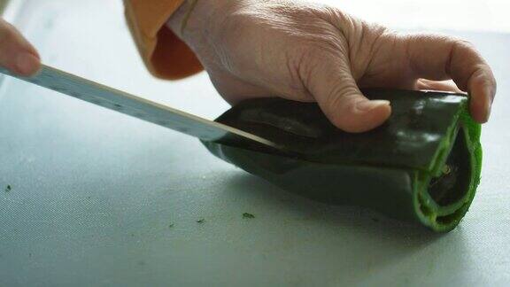 一位年长的白人妇女用菜刀在切菜板上切并清洗波布拉诺辣椒