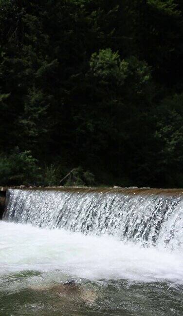 一个赤裸上身的男人微笑着站在瀑布背景下的山河中在水里擦脸垂直视频