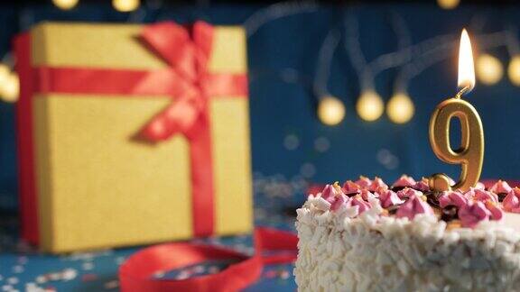 9号白色生日蛋糕金色蜡烛用打火机点燃蓝色背景用彩灯和黄色礼盒用红丝带绑起来特写镜头