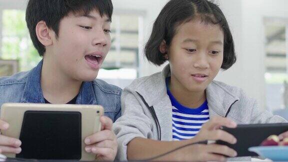 近距离的亚洲可爱的女孩和年轻的男孩玩在智能手机和平板电脑上的竞争视频游戏在横向横向模式中持有他们60帧秒摄影