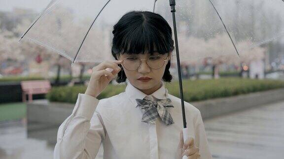 可爱的亚洲女生穿着校服打着伞站在街上