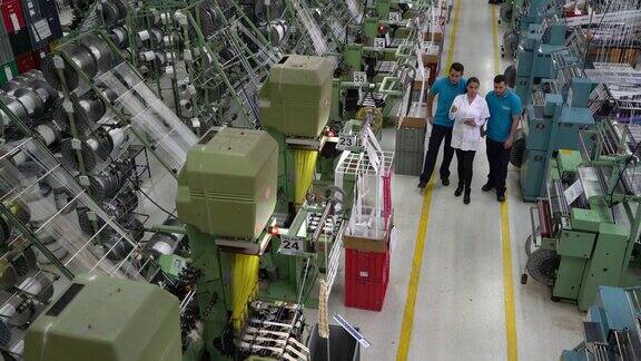 主管指导手工工人在生产线上拿着一块平板指着一台胶带工厂的机器