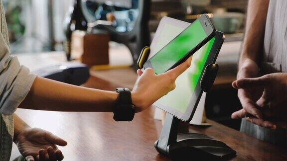 近距离的顾客使用移动钱包应用程序支付在绿色屏幕的平板电脑在咖啡厅柜台酒吧无线支付NFC生活方式