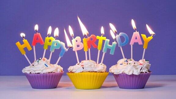 以紫色为背景在美味的纸杯蛋糕上用燃烧的彩色蜡烛刻上生日快乐的题词生日快乐视频横幅慢动作