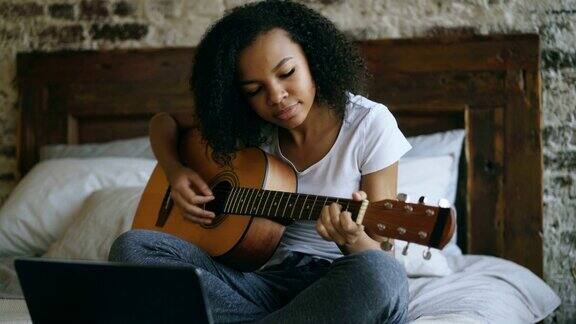 非洲裔少女学习弹吉他坐在家里的床上