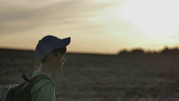 一个背着背包的男孩在日落时分在户外的平原上旅行