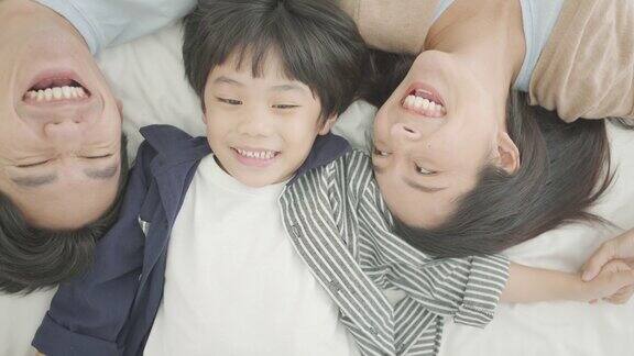 前视图幸福的亚洲家庭在温馨的家里爸爸妈妈和可爱的儿子一起在舒适的床上玩耍笑着放松在休闲的卧室里放松的一天家庭生活爱情情感关怀关系