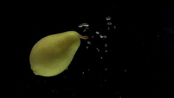 慢动作一个梨落在透明的水在黑色的背景