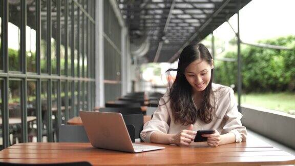 年轻女子在咖啡馆用手提电脑玩手机