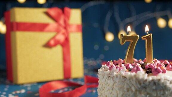 71号白色生日蛋糕金色蜡烛用打火机点燃蓝色背景用彩灯和黄色礼盒用红丝带绑起来特写镜头