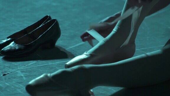 在聚光灯下芭蕾舞女演员将丝带系在脚上穿上投影仪上的尖头鞋