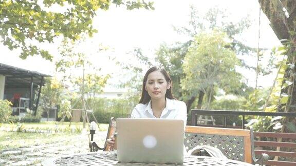 亚洲女人在花园里用笔记本电脑慢镜头