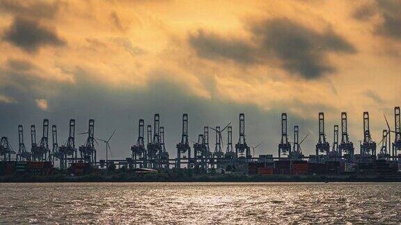 日落时分德国汉堡阳光照耀下的云天集装箱货运码头上有港口起重机和风力涡轮机