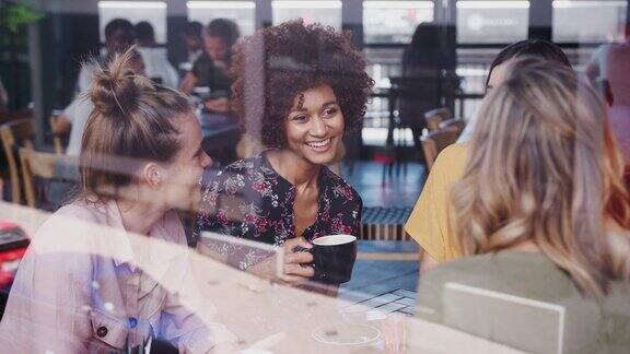 一群年轻的女性朋友聚在一起围坐在桌旁聊天透过窗户用慢动作拍摄