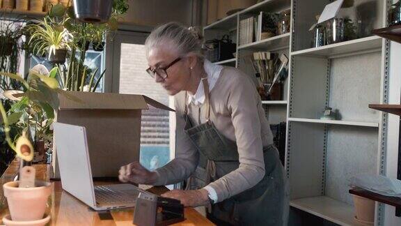 一名老妇人在工作时把订单装进盒子里检查笔记本电脑的4k视频