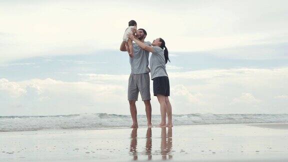 快乐的亚洲父亲母亲婴儿儿子有乐趣沿海边日落海浪在沙滩上积极的父母和人在暑假带宝宝户外活动幸福的家庭假期家庭、生活方式、人、人寿保险、假期