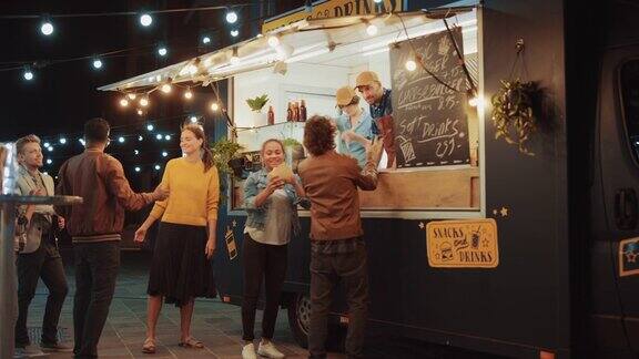 快餐车员工向在外面开派对的快乐的年轻嬉皮士顾客分发新鲜制作的汉堡、薯条和饮料一辆商业卡车在一个现代酷的街区卖街头食品