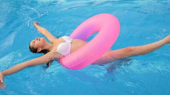 夏天的周末在泳池边穿着泳衣的女性漂浮在粉红色的充气环上