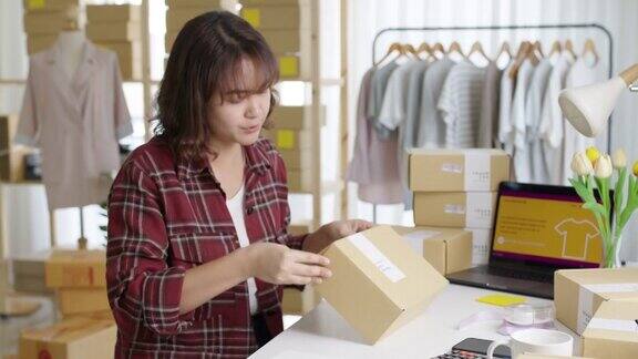 年轻有吸引力的美丽时髦的亚洲女性包装产品小商包裹订购网上零售商店交付给客户中小企业业主工作准备dropshipping箱在家办公室