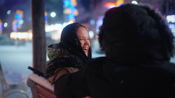 年轻的情侣约会和坐在长椅上聊天而在城市的雪晚上