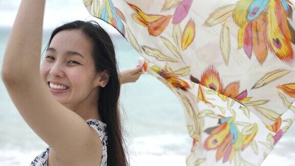 年轻快乐的女人在沙滩上伸出手围巾慢镜头