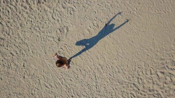 无人机拍摄的女人在做瑜伽动作在沙滩上投下阴影