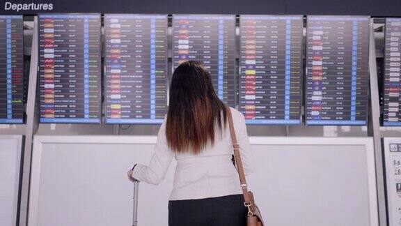 机场女商人亚洲女商人在屏幕上查看她的商务旅行的航班时间带着行李背包和笔记本电脑后视图