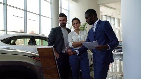 一对幸福的夫妇注意黑人推销员在谈论汽车经销商的财产